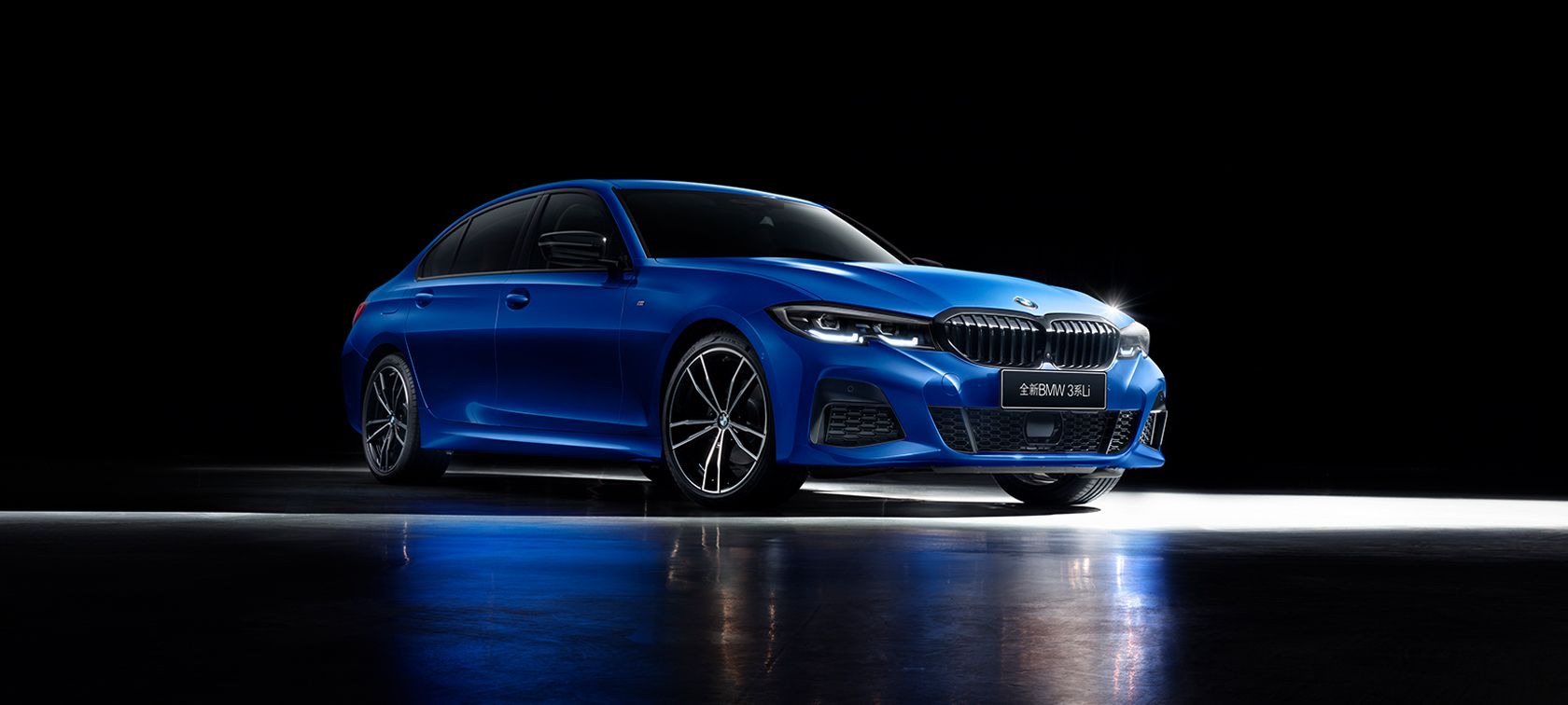 运动豪华,本色过人 Three-quarter side shot of the BMW 3 Series Sedan on asphalt in front of an urban backround with passengers.